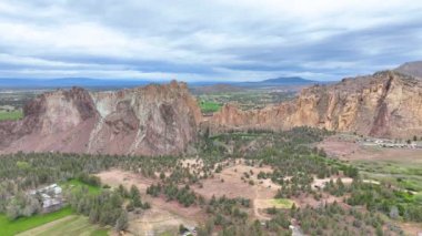 Hava İzleme Çekimi, Amerika Birleşik Devletleri, Oregon, Terrebonne, Smith Rock State Park dramatik kaya oluşumları, yemyeşil bitki örtüsü ve yumuşak bulutlu gökyüzü altında kıvrılan bir nehir sergiliyor.