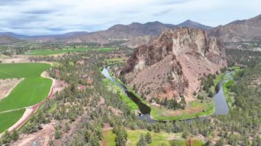 Oregon 'daki Smith Rock State Park' ın hava görüntüsü engebeli kaya oluşumları, kıvrımlı Eğri Nehir ve parçalı bulutlu gökyüzü altında yemyeşil alanlar gösteriyor. Turizm için ideal