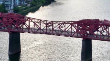 Hava Sabit Çekim: Gündüz gözüyle Portlands ikonik kırmızı Broadway Köprüsü 'nün modern yüksek binalar ve yemyeşil alanlar tarafından çerçevelenmiş durgun Willamette Nehri boyunca uzanan görüntüsü, kentsel cazibe ve