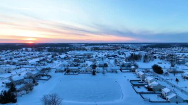 Gün doğumunda Fort Wayne, Indiana 'da sakin, karla kaplı bir muhitin hava yayı çekimi. Altın ışınlar evlerin sıralarını, sessiz caddeleri ve karla kaplı bir göleti aydınlatarak huzurlu bir kış yaratıyor.