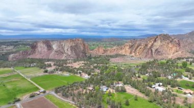 Terrebonne, Oregon 'daki Smith Rock State Park' ın hava izleme görüntüsü. Yükselen kaya tepeleri ve engebeli uçurumlar, aşağıdaki yemyeşil ve tarım arazileriyle zıt, yumuşak, bulutlu bir gündüz gökyüzünün altında,