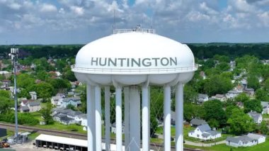 Hava Arc Shot: İndiana 'daki Huntington Su Kulesi' ni verimli yeşillik ve açık gökyüzü ile birlikte manzaralı bir banliyö manzarası altında ele geçirmek. Video, kasabaların yerleşim planlarını, demiryollarını ve tarihi yerleri vurguluyor.
