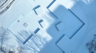 Aerial Top-Down Shot: Fort Wayne Indiana 'daki Freimann Meydanı' nda sakin kış sahnesi kar kaplı geometrik yapılar ve sakin mavi gökyüzü boyunca ağaçlar ve patikaların çerçevelediği el değmemiş karlar sergileniyor
