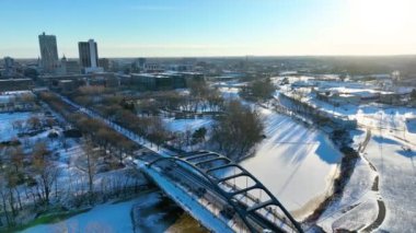 Aerial Fly Through Forward, ABD, Indiana, Fort Wayne: Martin Luther King Köprüsü 'nün kısmen donmuş bir nehir boyunca uzanan manzaralı görüntüsü, Promenade Park karla kaplanmış ve şehir