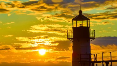 Siluetteki St. Joseph North Pier Deniz Feneri 'nin canlı Michigan Gölü günbatımına karşı nefes kesici hava manzarası. Altın saat ışığı, sakin sahil atmosferini güçlendirir.