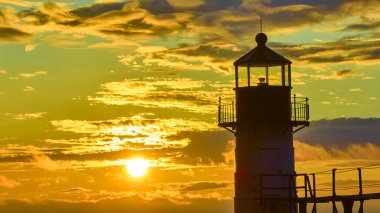 Breathtaking aerial view of the St. Joseph North Pier Lighthouse in silhouette against a vibrant Lake Michigan sunset. The golden hour light enhances the serene coastal atmosphere, symbolizing clipart