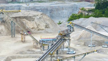 Expansive aerial view of an industrial quarry in Fort Wayne, Indiana. Showcasing intricate conveyor belts, heavy machinery, and active excavation operations against a backdrop of green foliage. clipart