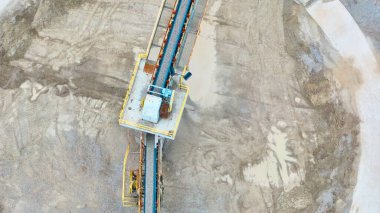 Fort Wayne, Indiana taş ocağındaki endüstriyel taşıma bandı sisteminin hava görüntüsü. Çakıl ve toprakla çevrili makineler, açık bir günde işyeri güvenliği ve ağır araç hareketini vurguluyor.