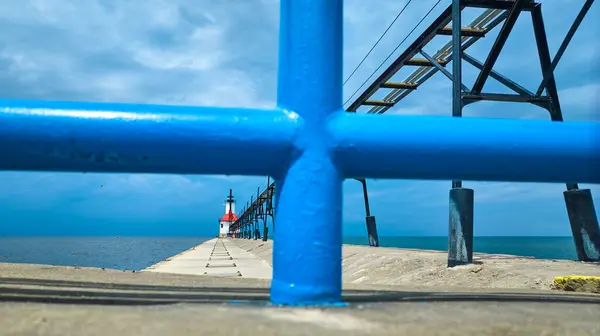 stock image St. Joseph North Pier Inner Lighthouse stands resilient at the end of a weathered pier on Lake Michigan, framed by a vibrant blue railing. The overcast sky adds a touch of solitude to this coastal