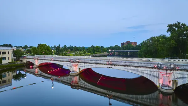 stock image Aerial view of River Lights Plaza in South Bend, Indiana, showcasing a beautifully lit bridge with red lights reflecting on a tranquil river during the blue hour, blending urban architecture with