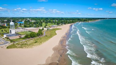 Aerial view of a serene beach in Kenosha, Wisconsin, along Lake Michigan. Bright blue sky, fluffy clouds, and gentle waves create a tranquil summer vibe. Perfect for tourism and real estate promotions clipart