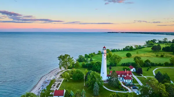 stock image Aerial view of Wind Point Lighthouse at sunset on the lush coastline of Lake Michigan in Wisconsin. The iconic white lighthouse with a red top stands tall, surrounded by charming buildings and