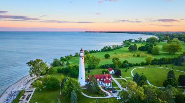 Günbatımında Wisconsin 'deki Rüzgâr Noktası Deniz Feneri' nin hava manzarası. Kırmızı çatılı tarihi deniz feneri Michigan Gölü kıyı şeridi boyunca duruyor, yemyeşil ve tuhaf binalarla çevrili..