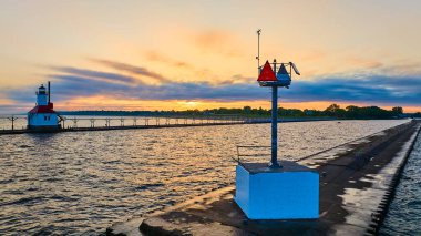 Serene golden hour at Benton Harbors North Pier. The red-roofed lighthouse reflects on Lake Michigan, with a navigational marker adding a maritime touch. Perfect coastal scene for travel and maritime clipart