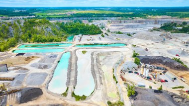 Fort Wayne, Indiana 'da, turkuaz su kuyuları, endüstriyel makineler ve canlı kamyonlarla genişleyen bir taş ocağının hava görüntüsü. Bereketli yeşil arazi sanayi operasyonlarıyla çelişiyor.