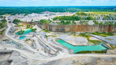 Fort Wayne, Indiana 'da geniş bir taş ocağının havadan görünüşü, teraslı kaya oluşumları, turkuaz su kütleleri ve yemyeşil alanların ortasında ağır makineler. Endüstriyel faaliyet doğal ile buluşur
