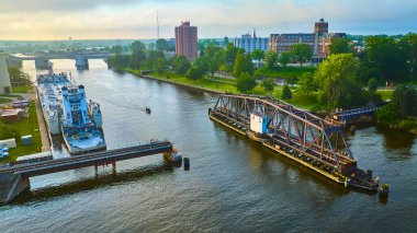 Benton Limanı 'nın hareketli nehir kenti havadan görünüşü St. Joseph Nehri' ni geçen bir kargo gemisi, geçiş için açılan çelik bir kiriş köprüsü ve sakin sabah ışığında kentsel mimari..