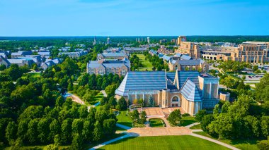 Aerial view of Notre Dame University in South Bend, Indiana, showcasing the Performing Arts Center, lush landscapes, and iconic architecture. Ideal for educational or urban planning materials. clipart