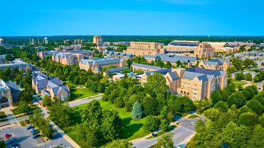 South Bend, Indiana 'daki Notre Dame Üniversitesi kampüsünün geniş hava manzarası. Akademik binalar, yemyeşil alanlar ve açık mavi gökyüzünün altında büyük bir stadyum. Eğitim ve öğretim için ideal
