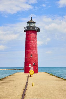 Kenosha, Wisconsin 'deki Michigan Gölü' ndeki beton iskelenin sonunda canlı kırmızı deniz feneri duruyor. Açık mavi gökyüzü ve sakin sular seyahat broşürleri için mükemmel sakin bir sahil manzarası yaratır.