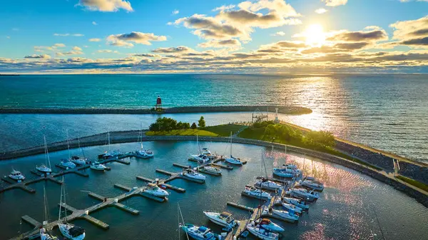 Altın saat boyunca Wisconsin 'deki Racine South Pier Marina' nın havadan görüntüsü. Güneş sakin suların üzerinde batıyor. Yelkenli ve deniz fenerini yansıtıyor. Bu güzel limanın huzur dolu güzelliğini vurguluyor..