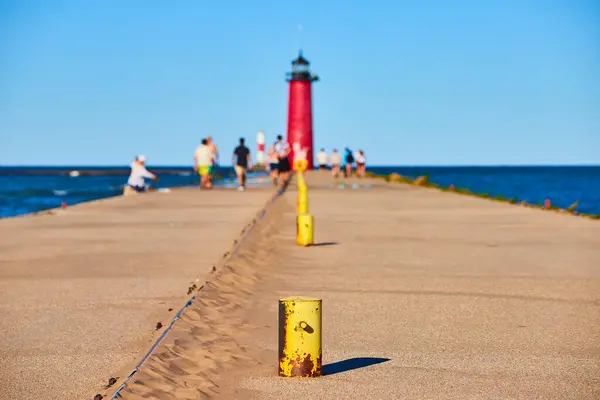 stock image Stroll along the Kenosha Pier, guided by vibrant yellow bollards, towards the striking red Kenosha Lighthouse with Lake Michigans serene blue waters and a clear sky creating a tranquil coastal scene