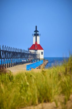 Benton Limanı 'nın Michigan Gölü' ndeki iç deniz fenerinin sakin manzarası, açık mavi gökyüzüne karşı duran kırmızı çatılı bir fener. Endüstriyel rıhtım deniz fenerine gidiyor, sükuneti yakalıyor ve...