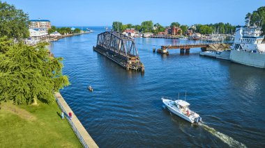 Aerial view of Benton Harbor, Michigan featuring the historic iron drawbridge over the St. Joseph River, a modern yacht cruising by, and the scenic West Basin Marina on a bright sunny day. Perfect for clipart