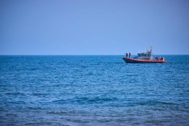 Sahil Güvenlik teknesi Benton Limanı yakınlarındaki Michigan Gölü 'nün sakin sularında geziniyor. Mürettebattan iki kişi açık denizde mavi bir gökyüzünün altında tema ve ihtiyatı ön plana çıkarıyor.
