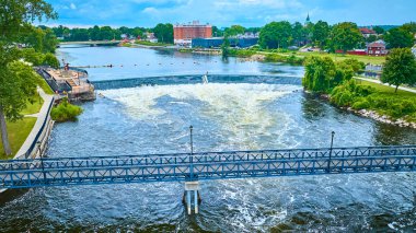 Mishawaka St. Joseph Nehri 'nin hava manzarası. Güçlü alçak başlıklı bir baraj ve çarpan mavi yaya köprüsü var. Manzaralı nehir kenarı şehir manzarası yemyeşil, tarihi mimari ve