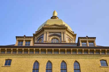 South Bend 'deki Notre Dame Ana Binası' nın ikonik altın kubbesi, tarihi mimari güzelliği ve akademik mirası sergileyen açık mavi gökyüzüne karşı görkemli bir şekilde duruyor. Mükemmel.