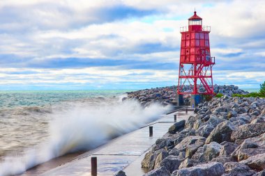 Kırmızı deniz feneri Racine, Wisconsin 'deki kayalık bir iskelede güçlü dalgaların Michigan Gölü' nün serin ve bulutlu bir sabahında kıyıya çarpmasıyla esnek duruyor. Kararlılığın ve doğanın sembolü.