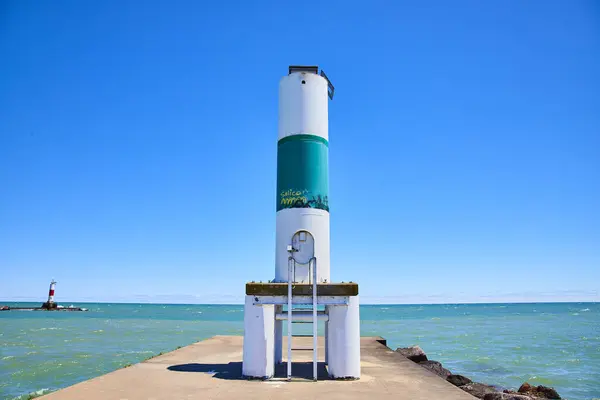 stock image Serene view of a white and green day beacon on a concrete pier at Lake Michigan, Kenosha, Wisconsin, with a smaller lighthouse in the distance and a clear blue sky above. Ideal for themes of