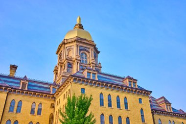 South Bend, Indiana 'daki Notre Dame Üniversitesi' nin ana binasının altın kubbesi. Öğleden sonra ışığı ve açık mavi gökyüzü ile alçak bir açıdan çekilmiş, tarihi mimarisini vurguluyor.