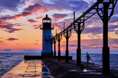 Benton Harbors Outer Lighthouse stands tall on Lake Michigan North Pier at sunset. The warm hues of golden hour paint a serene coastal scene, reflecting beauty and tranquility in the wet pier surface clipart