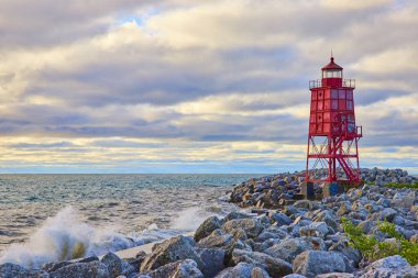 Gün doğumunda Michigan Gölü 'ndeki Racine Kırık Su Deniz Feneri' nin engebeli güzelliği. Dalgalar kayalık kıyı şeridine çarparak, deniz fenerlerini parlak kırmızı gökyüzüne vuruyor. Wisconsin, ABD