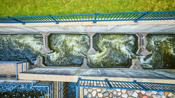 stock image Aerial view of a dynamic water management structure in Mishawaka, Indiana, showcasing a fish ladder, concrete barriers, and blue metal railings. Turbulent water flows through, highlighting