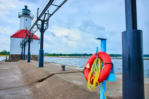 stock image Tranquil scene at North Pier in St. Joseph, Michigan: Lighthouse with red roof, bright life buoy on a blue stand, and overcast sky, emphasizing maritime safety on the shores of Lake Michigan.