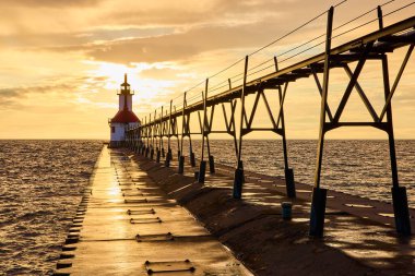 Benton Limanı Kuzey İskelesi, Michigan Gölü 'nde altın saat. İkonik beyaz ve kırmızı deniz feneri, sakin sulardan yansıyan sıcak ve sakin bir gökyüzünün altında gemilere yol gösteriyor. Huzur