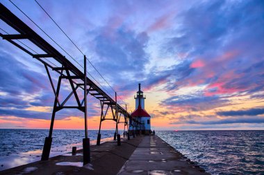 Michigan Gölü üzerinde sakin bir gün batımı. Islak iskele sonunda Benton Limanı Deniz feneri, canlı gökyüzü renklerini yansıtıyor. Seyahat, turizm ve ilham verici içerik için mükemmel..
