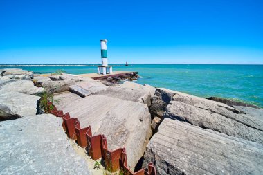 Kenosha, Wisconsin 'deki Michigan Gölü' nün sakin sahili. Beton bir iskelede duran beyaz ve yeşil bir işaret, açık mavi bir gökyüzünün altında denizlerde yol gösteriyor. Seyahat ve sahil şehri için mükemmel.