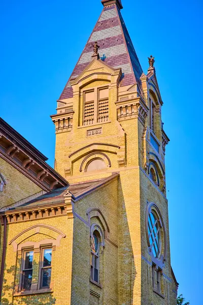 Notre Dame Üniversitesi, South Bend 'in tarihi saat kulesi. 1881 'deki sarı tuğla yapıda süslü detaylar ve dik, zarif bir çatı bulunur. Parlak mavi gökyüzü mimarisini vurguluyor