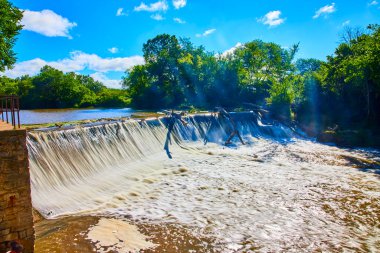 Root River Barajı 'nın sakin manzarası Racine, Wisconsin' de, yemyeşil bir şelalede şelale gibi akıyor. Güneş ışığı ağaçların arasından süzülüp, doğa için mükemmel, sakin ve büyülü bir atmosfer yaratır.