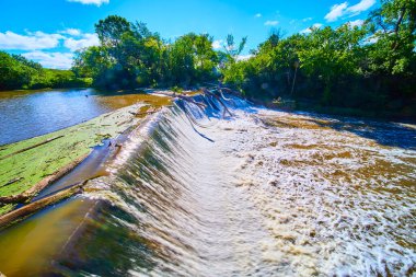 Racine, Wisconsin 'deki Baraj Root Nehri üzerinde sakin bir şelale. Yeşillik ve güneş ışığıyla çevrili bu sakin sahne doğal güzellik ve dinamik enerjinin özünü yakalar..