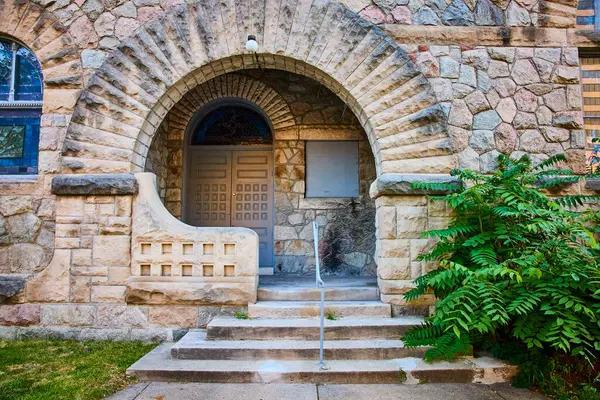 stock image Grand arched entrance to a historical stone building in downtown South Bend, Indiana. Meticulous stonework, decorative stained glass, and urban greenery create a timeless blend of architecture and