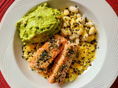 Sağlıklı ve canlı bir somon tabağı. Kırmızı dokuma altlığında avokado püresi ve beyaz fasulye. Beslenme ve gurme pişirme için mükemmel. Fort Wayne, Indiana 'da ele geçirildi.