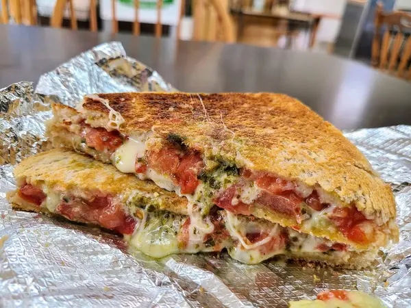 Fort Wayne, Indiana 'da ağız sulandıran ızgara peynirli sandviçin yakın çekimi. Erimiş peynir, sulu domatesler ve mükemmel kızarmış ekmeğin arasına yayılmış yeşil bir pesto. Mükemmel rahatlık