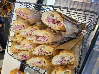 Kahverengi kağıda sarılmış, Portland 'daki bir fırında sergilenen yeni hazırlanmış jambonlu peynirli baget sandviçler. Altın kabuk ve cömert dolgu bu zanaatkar yiyecekleri bir gurme için mükemmel yapıyor.