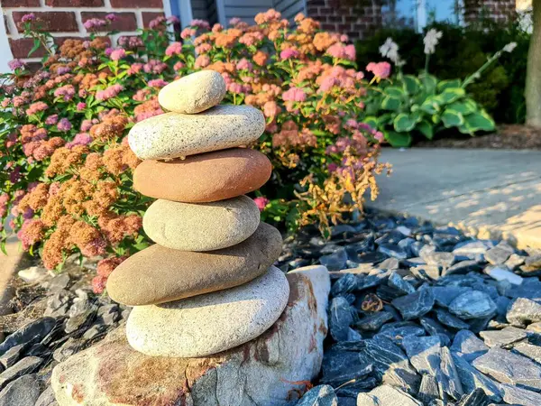 stock image Zen stone stack in a tranquil suburban garden in Fort Wayne, Indiana. Smooth stones balanced in harmony among vibrant flowers during the golden hour, perfect for themes of mindfulness and relaxation.