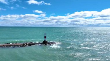 Kenosha Deniz Feneri, Kenosha, Wisconsin 'deki Michigan Gölü' ndeki dalgalı bir dalgakıranın sonunda dirençli bir şekilde duruyor. Turkuaz suyla çevrili, rehberliği ve yalnızlığı sembolize eder.